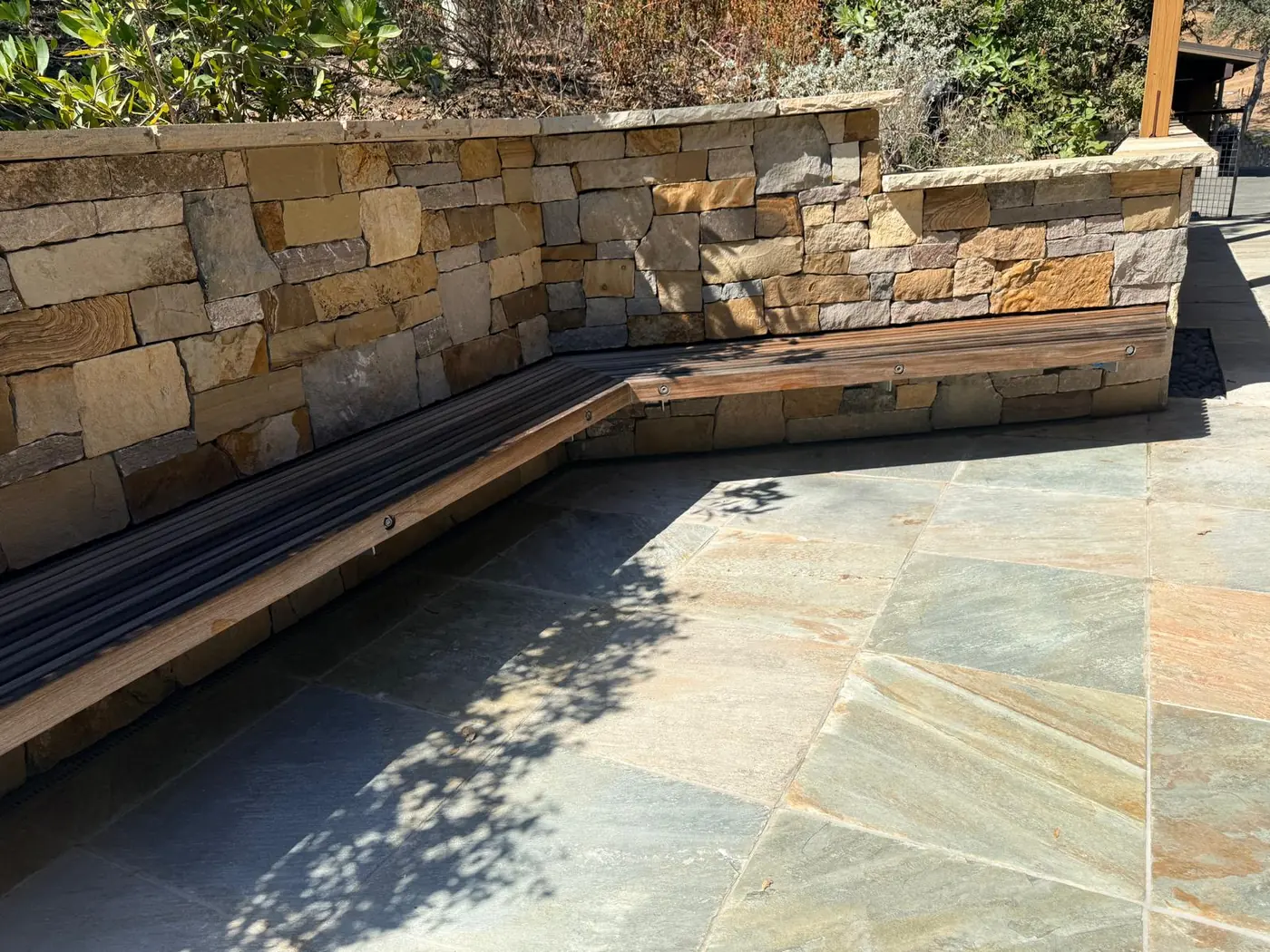 Stacked natural stone wall with a built-in bench over a flagstone patio